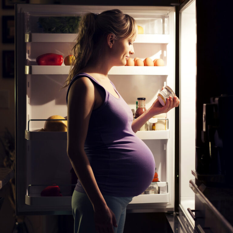An expectant mother carefully selecting healthy food options from an open refrigerator.